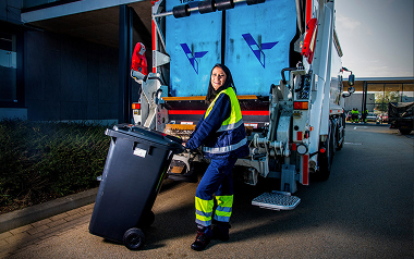 Vrouw met afvalbak naast vuilniswagen op straat!