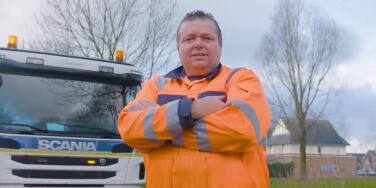 Persoon in oranje veiligheidskleding staat voor een vrachtwagen.