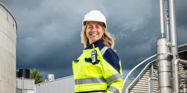 Persoon in een oranje veiligheidsjas staat in een overdekte ruimte voor een grote witte vrachtwagen met AREA‑opschrift.
