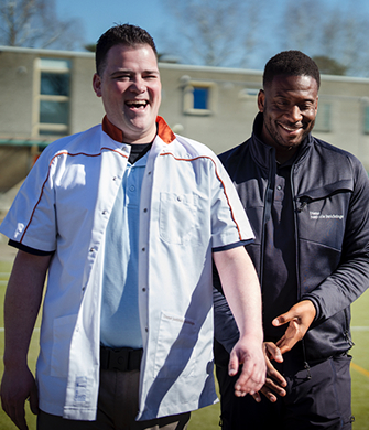 Twee personen lopen samen op een sportveld.