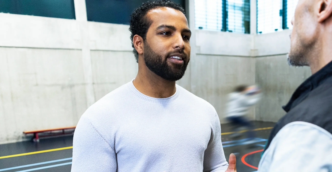 Twee mannen praten in sporthal tijdens activiteit.