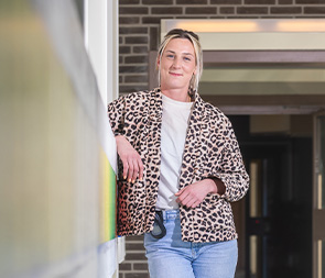 Vrouw leunt ontspannen bij ingang van gebouw hier