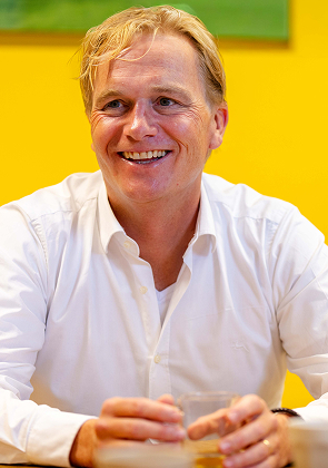 Lachende man zit aan tafel met drankje op kantoor