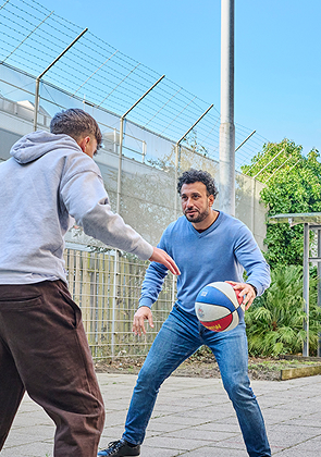 Man speelt basketbal met jongen op binnenplaats