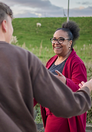 Jonge man en oudere vrouw lachen en praten enthousiast in weiland bij zonsondergang
