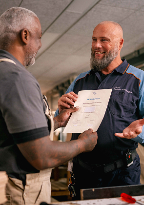 Medewerker overhandigt certificaat in werkplaats