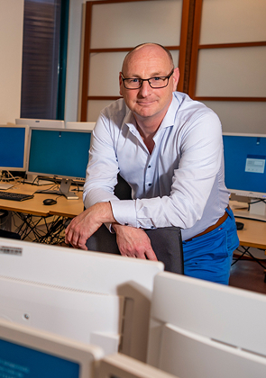 Man staat in computerlokaal tussen werkplekken