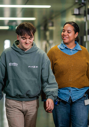 Begeleider loopt samen met jongere door gang