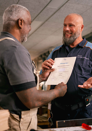 Medewerker overhandigt certificaat in werkplaats