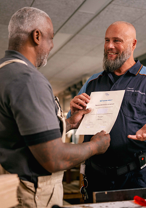 Medewerker overhandigt certificaat in werkplaats