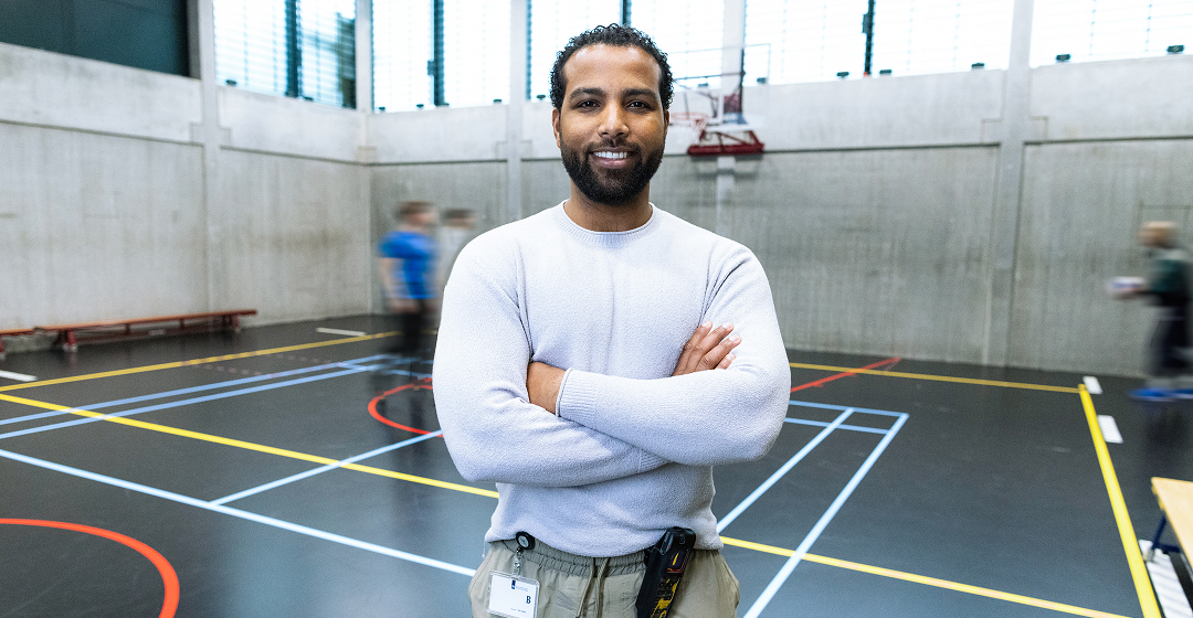 Man staat in sporthal met gekruiste armen en glimlacht