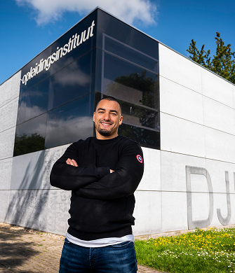Man staat met gekruiste armen voor gebouw