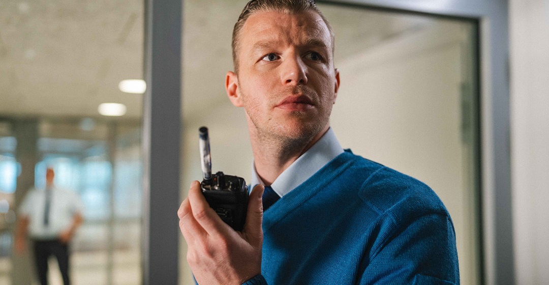 Man met portofoon kijkt waakzaam in kantoorruimte