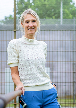 Vrouw leunt ontspannen tegen hek bij sportveld