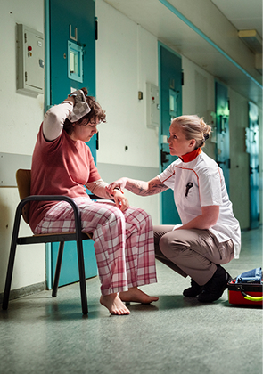 Zorgverlener helpt zittende vrouw in gang