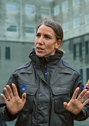 Vrouw in jas spreekt met handen omhoog buiten stad