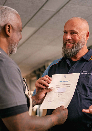 Medewerker overhandigt certificaat in werkplaats