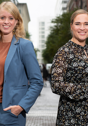 Twee collega’s poseren lachend in stadsstraat