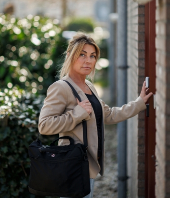 Persoon opent voordeur met tas over schouder