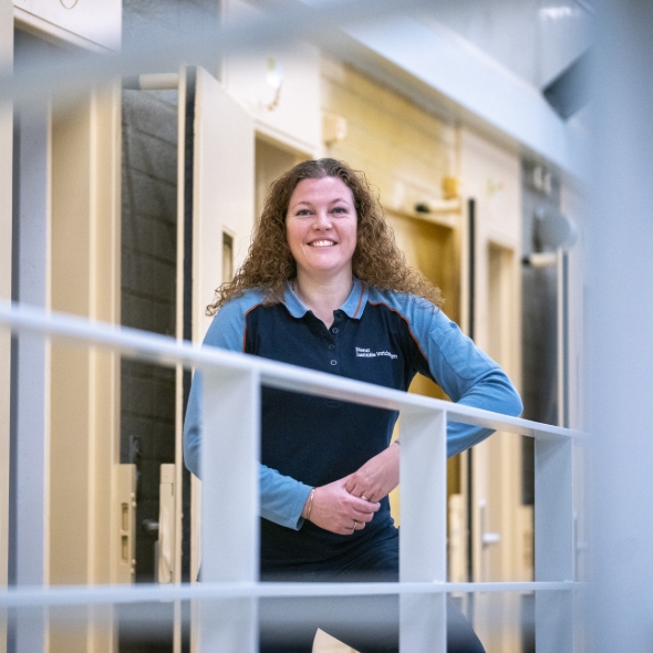 Vrouw in uniform staat glimlachend bij celgang