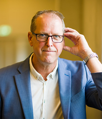 Man met bril in blauw colbert kijkt in camera