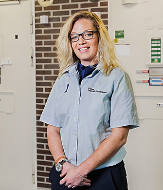 Vrouw in uniform staat glimlachend in werkomgeving