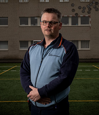 Man met bril staat op sportveld bij gebouw