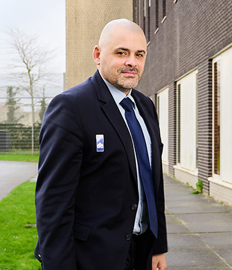 Man in pak staat buiten bij gebouw en kijkt naar camera