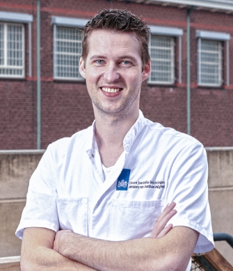 Een man in een witte jas staat in een gang van het Justitieel Centrum voor Somatische Zorg in Den Haag
