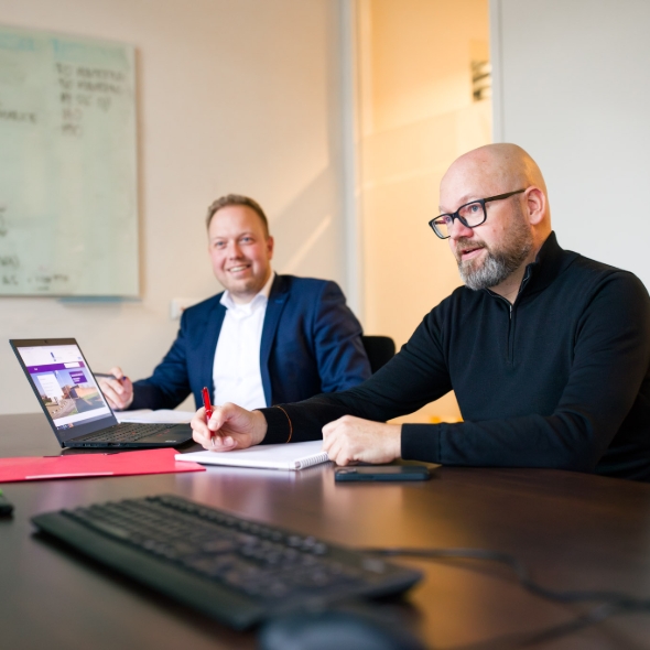 Drie mannen vergaderen actief aan tafel met laptop en notitieblok in modern kantoor