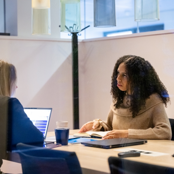 Twee vrouwen in gesprek aan tafel met laptop en koffie