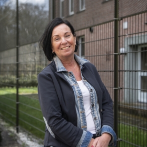 Een vrouw staat voor een gebouw en kijkt in de camera