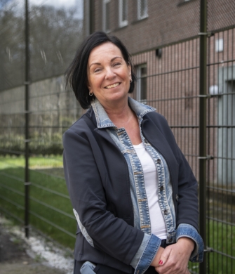 Een vrouw staat voor een gebouw en kijkt in de camera