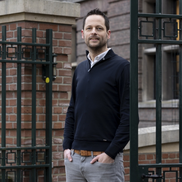 Man staat bij hek voor gebouw in buitenomgeving