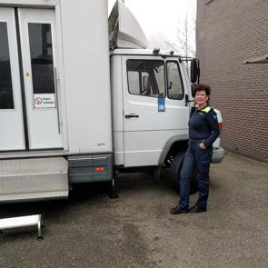 Een vrouw staat naast een bus en kijkt in de camera