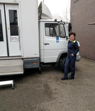 Een vrouw staat naast een bus en kijkt in de camera