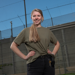 Persoon met handen op heupen bij hek buiten