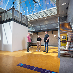 Drie mensen praten in modern atrium met trap