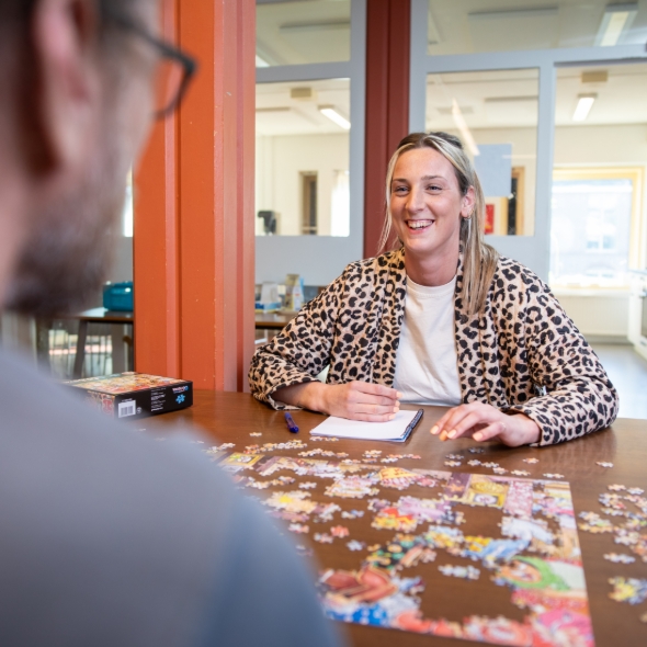 Jonge vrouw met luipaardjas doet puzzel en lacht vriendelijk