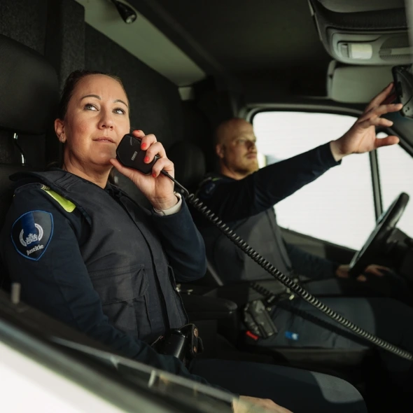 Twee justitiemedewerkers in voertuig met radio
