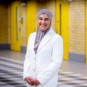 Een vrouw staat buiten bij een gebouw en kijkt in de camera