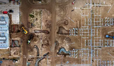 An aerial view of a construction site showing excavators, trenches, and building foundations in progress.