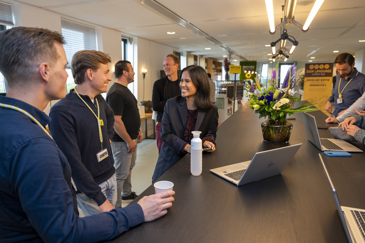 Two Stedin utility workers wearing safety helmets and high-visibility jackets inspect electrical panels inside a facility.
