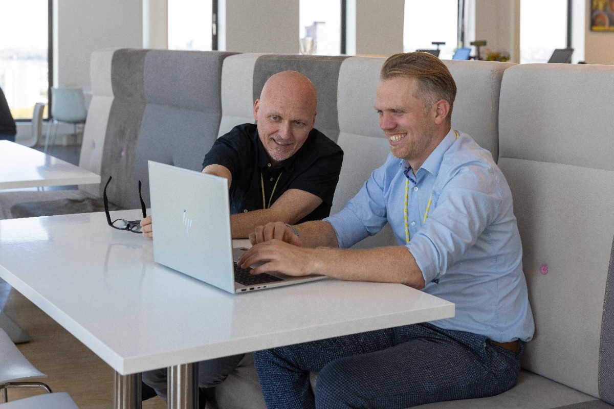 Two Stedin utility workers wearing safety helmets and high-visibility jackets inspect electrical panels inside a facility.