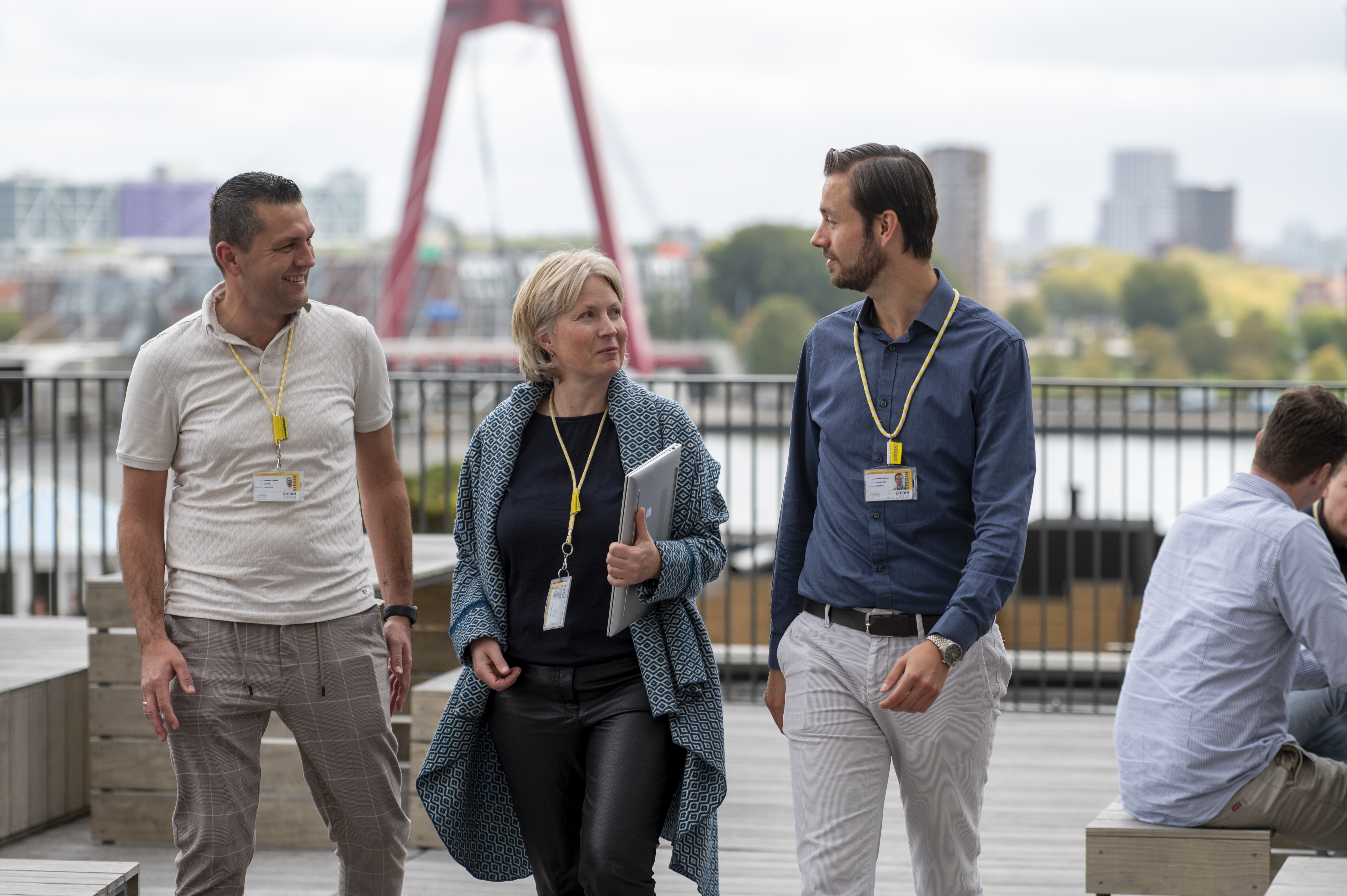 Two Stedin utility workers wearing safety helmets and high-visibility jackets inspect electrical panels inside a facility.