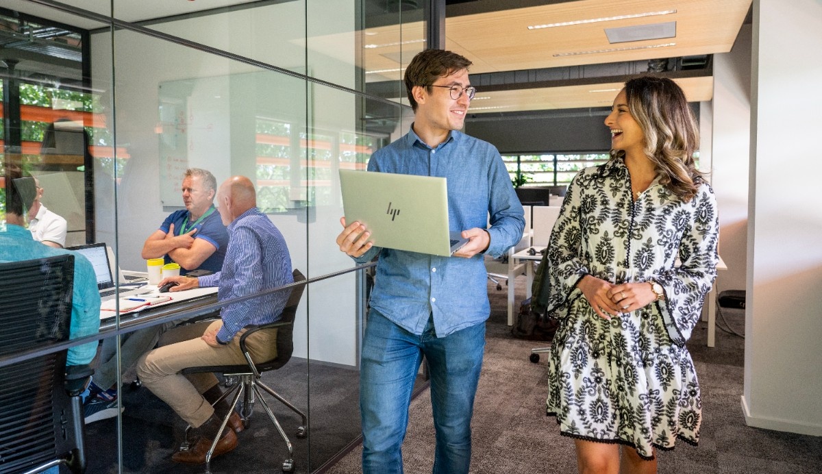 Two Stedin utility workers wearing safety helmets and high-visibility jackets inspect electrical panels inside a facility.