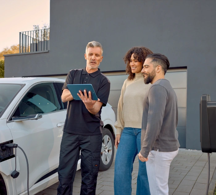 Three people reviewing tablet near electric car outdoors