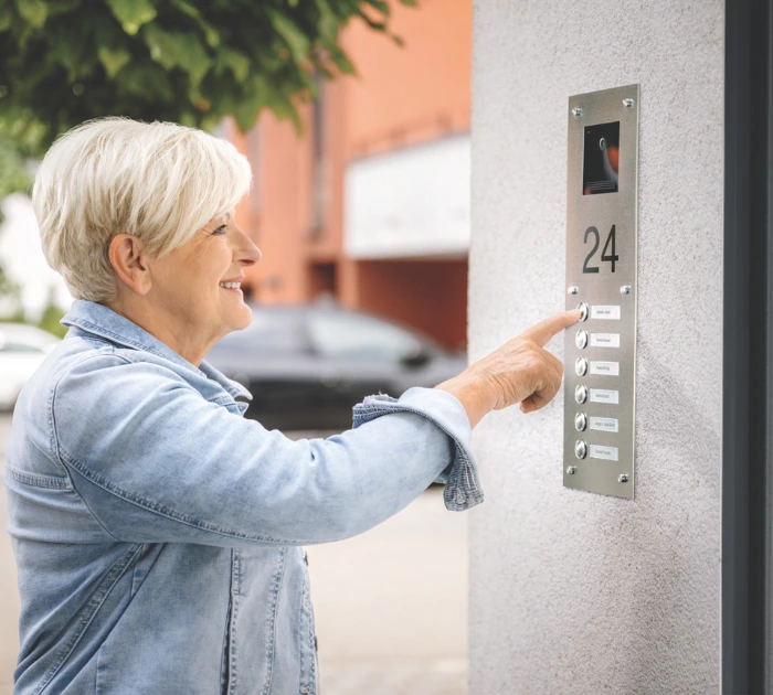 Woman pressing apartment intercom buttons outside building