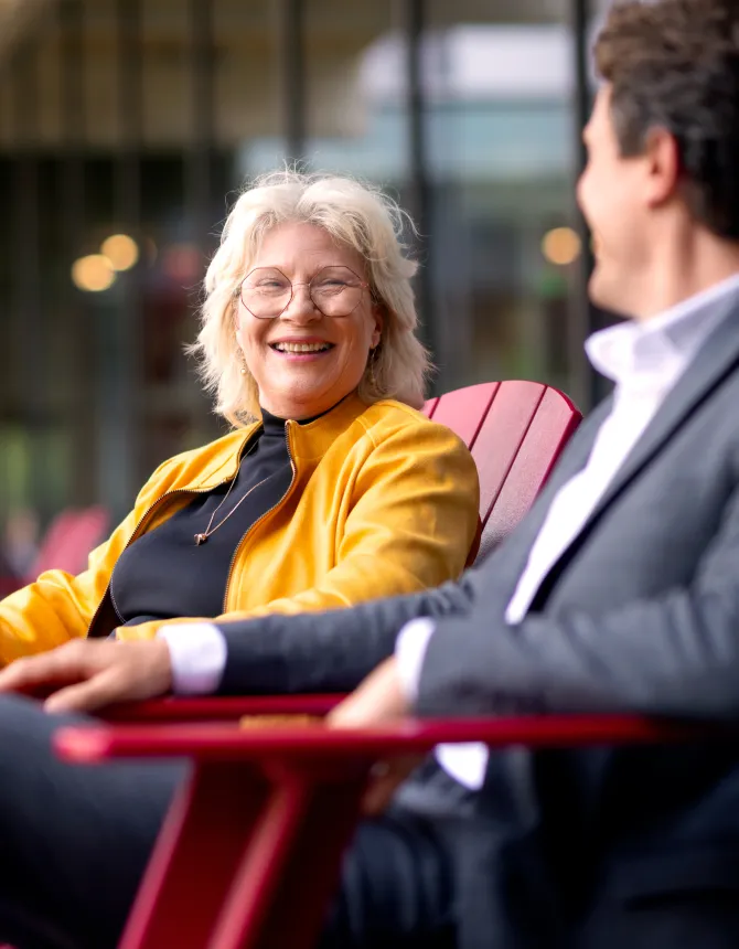 Twee collega's lachen samen op rode buitenstoelen