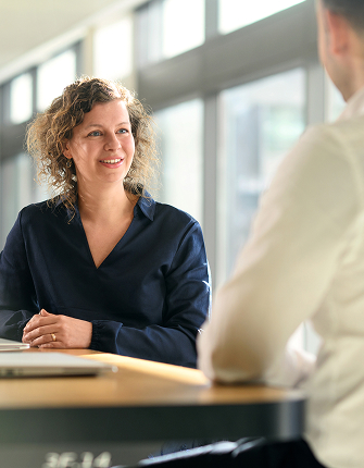 Vrouw glimlacht tijdens gesprek aan kantoortafel
